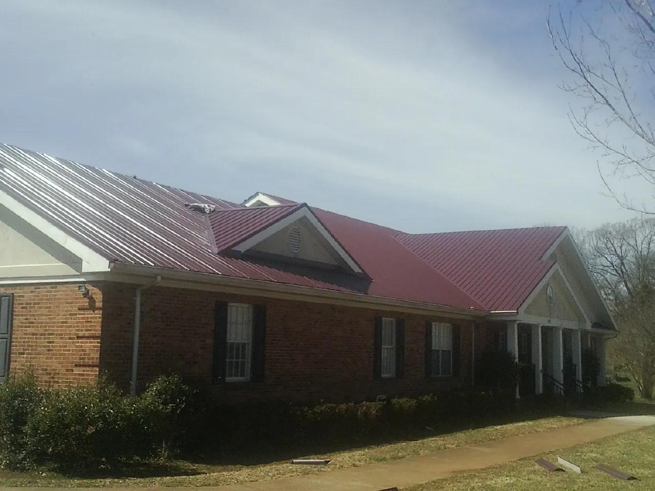 Red metal roof with gabled entries on a long brick building, from a Hail Damage Roof Repair job in Tylertown