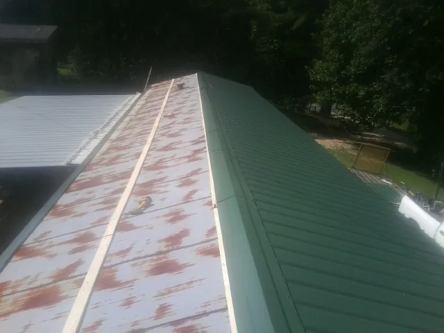 Old rusted panels beside newly installed green metal roofing — Wind Damage Roof Repair by Roofing Brothers in Tylertown