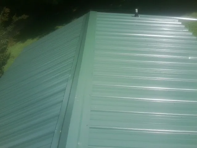 New green metal panels meeting at the ridge of a roof — Flat Roof Repair work by our crew in Tylertown
