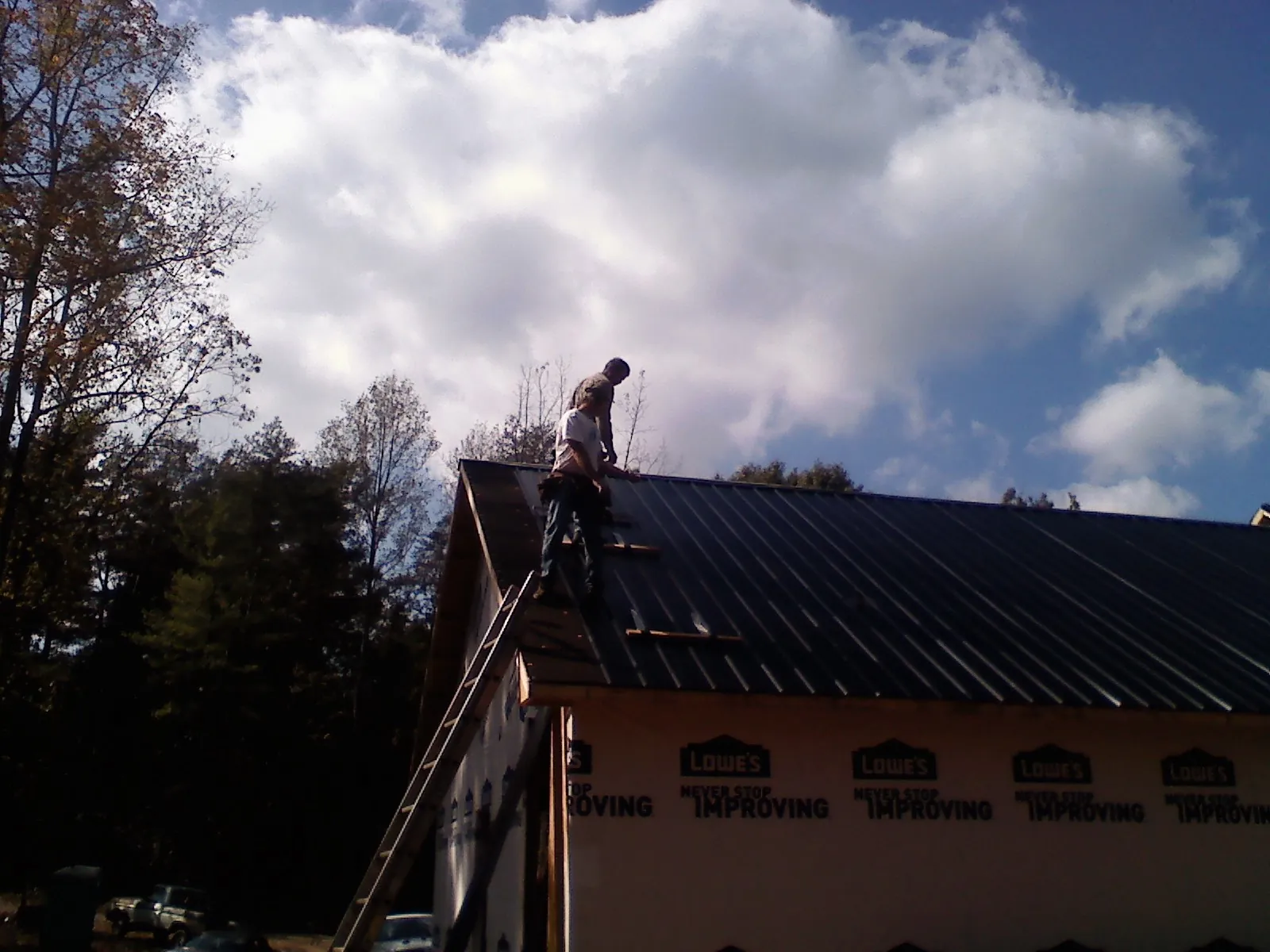 Roofer fastening dark metal panels high against a cloudy sky, from a Roof Inspection job in Tylertown