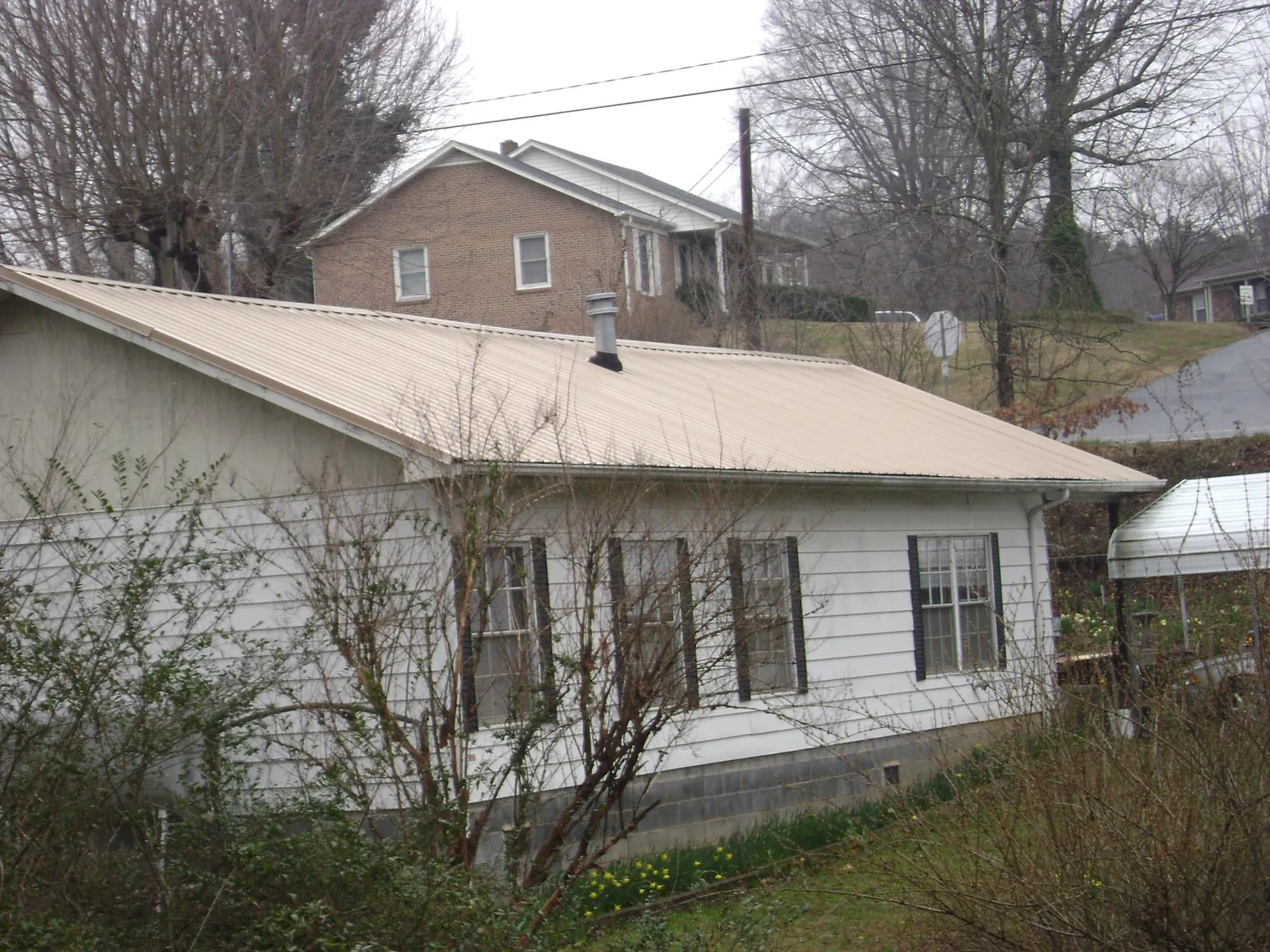 Tan metal roof on a white sided house set into a hillside — Commercial Roofing by Roofing Brothers in Tylertown