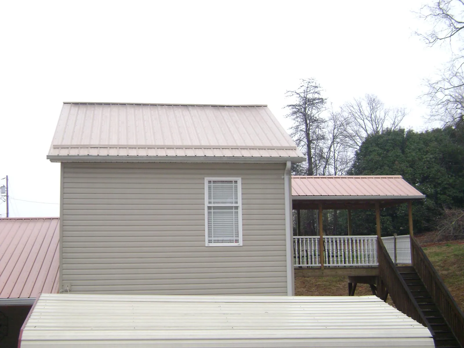 Tan metal roofs on a two story addition and attached porch, from a Roof Replacement job in Tylertown