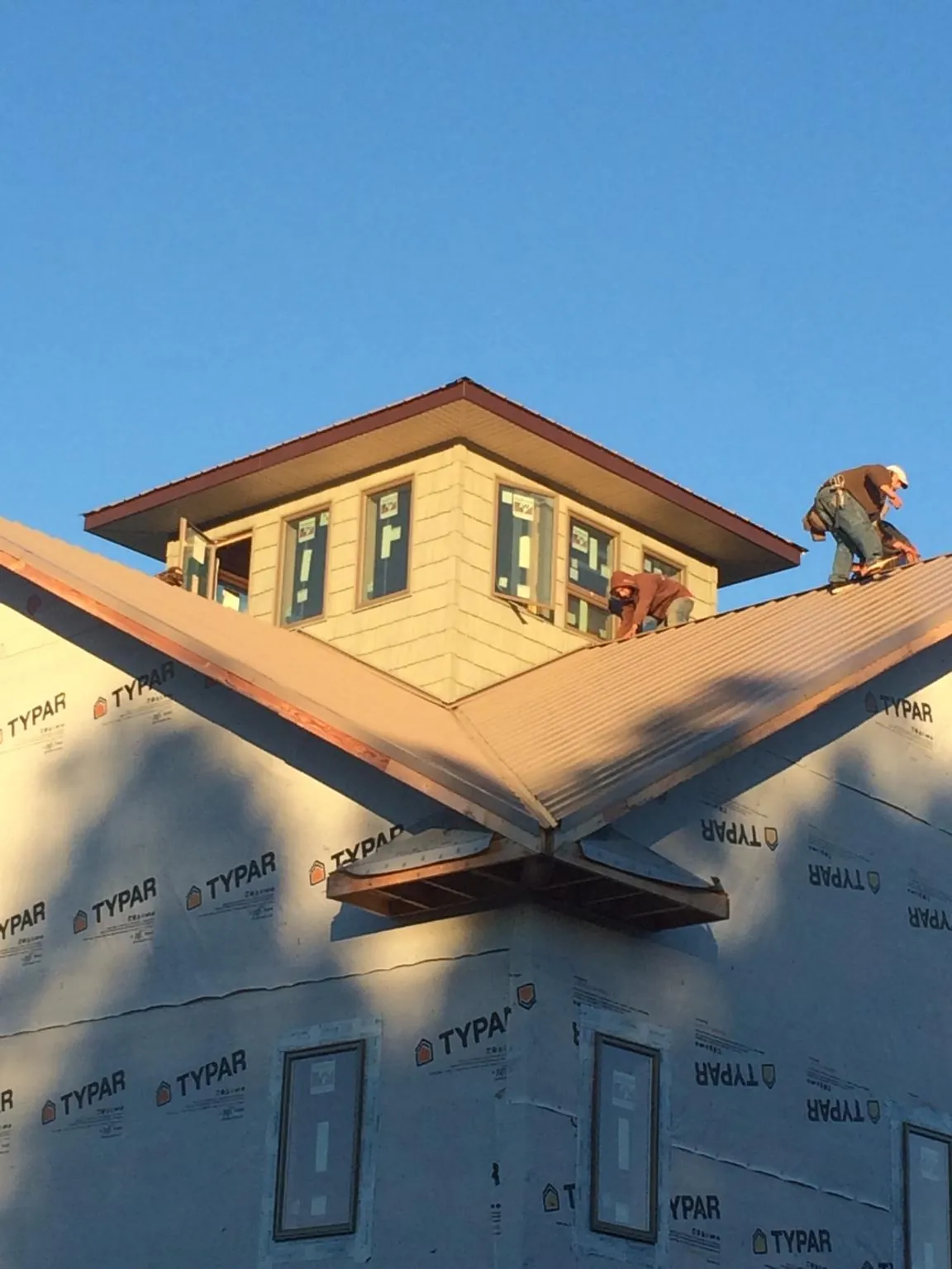 Roofers working around a rooftop cupola on a new metal roof at sunset — Roof Waterproofing in Tylertown by Roofing Brothers